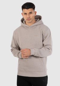 Lichtgrijze hoodie gemaakt van zachte stof, met een voorzak en ribgebreide manchetten. Klein logo op de borst voegt detail toe.