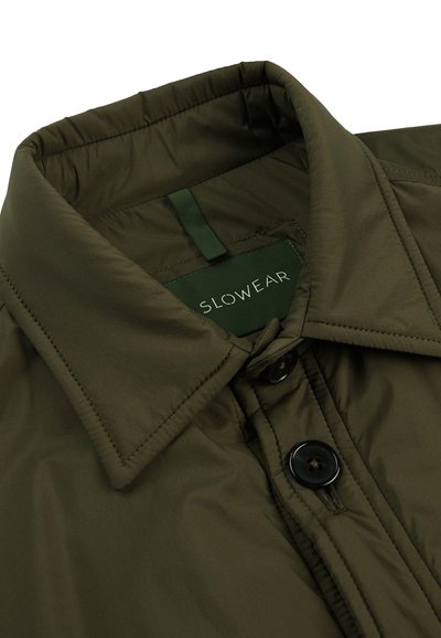 Chaqueta de plumas verde oliva con un cuello estructurado, etiqueta de marca y cierre de botón negro. Tejido suave y ligero con detalles de costura.