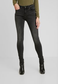 Calças de ganga skinny pretas com ligeira descoloração, apresentando um design de cinco bolsos e fecho éclair. Combinadas com botas pretas de salto.