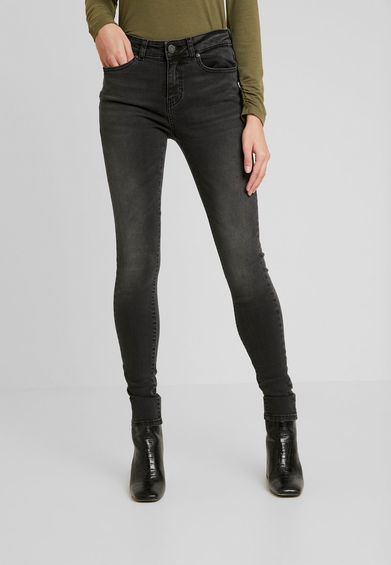 Calças de ganga skinny pretas com ligeira descoloração, apresentando um design de cinco bolsos e fecho éclair. Combinadas com botas pretas de salto.