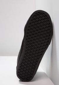 Czarna podeszwa sneakersa z karołowym bieżnikiem ustawiona pod kątem na białej powierzchni z narożnikami.