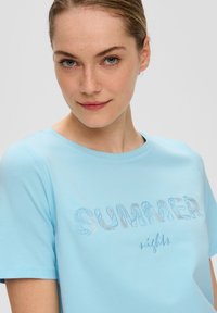 Camiseta de algodón de color azul claro con mangas cortas que presenta el texto bordado "NOCHES de VERANO" en varios colores. Textura suave, escote redondo.