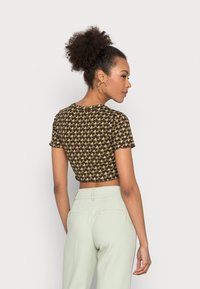 Brown cropped top with short sleeves featuring a geometric pattern in green and cream. Paired with light green high-waisted trousers.