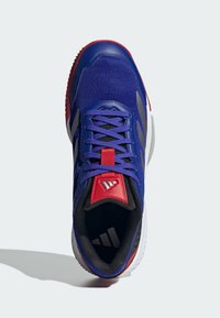 Chaussure de sport avec une tige en maille bleue, des accents rouges, une doublure noire, une semelle texturée et des bandes de marque argentées sur le côté.