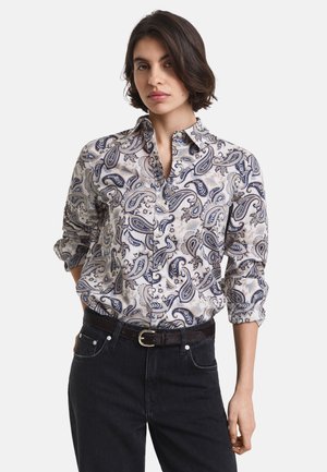 Camicia a maniche lunghe con bottoni di colore crema con motivo paisley blu navy. Presenta un colletto, maniche arrotolate e una vestibilità rilassata. Indossata con jeans scuri.