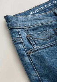Jeans de mezclilla en azul medio, con una textura desgastada, dos bolsillos y detalles en metal negro. La etiqueta dice "MOTION FLEX."