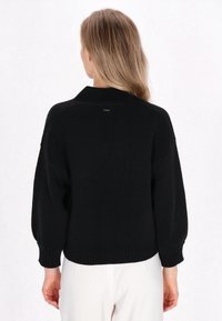 Maglione nero a maglia con vestibilità rilassata, spalle scese e polsini e orlo a coste. Include un piccolo dettaglio con logo sul retro.