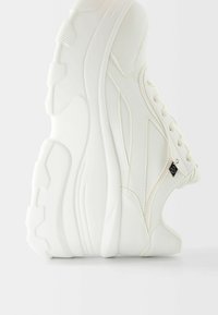 Sneaker bianco con tomaia in sintetico liscio, punta tonda, suola spessa e cuciture decorative. Presenta un piccolo logo nero sul lato.