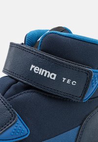 Námořnické textilní kotníkové boty s modrými akcenty. Obsahují suchý zip s brandingem "reima TEC" a texturované materiály pro lepší úchop.