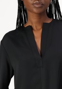 Maglietta nera con scollo a V profondo, maniche lunghe e una texture liscia con sottili dettagli di cucitura.