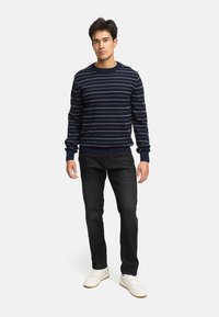 Mørkeblå stribet sweater med lys blå og cremefarvede striber, ribbede manchetter og kant, parret med sorte jeans og hvide sneakers.