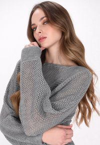 Maglione grigio lavorato a maglia con un motivo a trama aperta e rilassata. Presenta maniche lunghe e un ampio scollo, evidenziando una texture morbida.