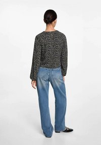 Zwarte blouse met bloemmotief en lange mouwen, gecombineerd met lichtblauwe wijde jeans. De blouse heeft een keyhole-detail op de rug.