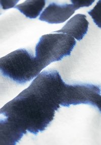 Gros plan d'un tissu blanc avec un motif tie-dye bleu et noir et une texture ainsi que des plis visibles.