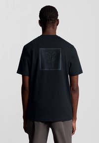 Zwarte katoenen t-shirt met ronde hals, voorzien van een gestructureerde afbeelding van een adelaar en "1874" bedrukt op de achterkant. Korte mouwen.