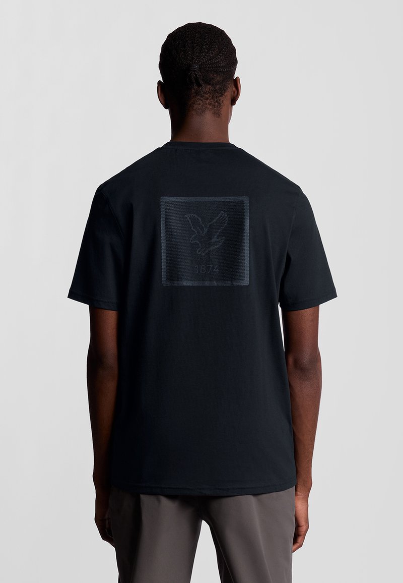 Zwarte katoenen t-shirt met ronde hals, voorzien van een gestructureerde afbeelding van een adelaar en "1874" bedrukt op de achterkant. Korte mouwen.