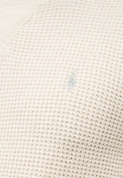 Ανοιχτό μπεζ πλεκτό πουλόβερ με υφή βαφλής, με μικρό, κεντημένο λογότυπο σε ασορτί ανοιχτό γκρι στο στήθος.