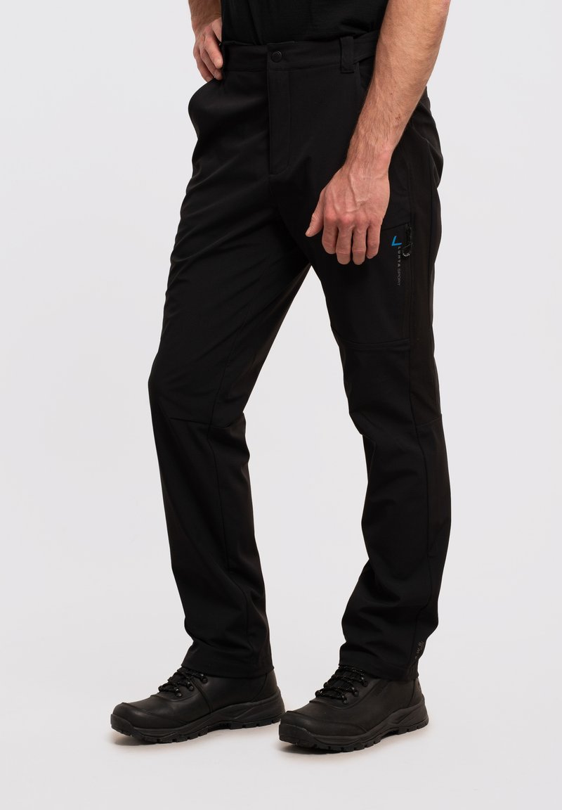 Schwarze Hose mit taillierter Passform, ausgestattet mit einer Reißverschlusstasche an der Seite und einer glatten Textur. Kombiniert mit schwarzem Schuhwerk, wobei der Schwerpunkt auf Funktionalität liegt.
