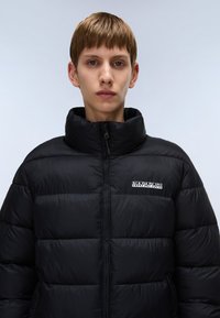 Jachetă puffer neagră cu guler înalt și închidere cu fermoar. Prezintă un design matlasat și un mic logo alb pe piept. Textură netedă.