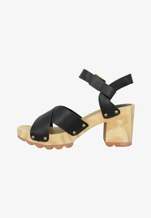 Sandale à talon en cuir noir avec des brides entrecroisées, base en bois et accents en matériel doré. Présente un talon épais et une semelle à bords festonnés.