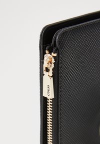 Portafoglio nero testurizzato con chiusura a zip dorata e etichetta con marchio. Presenta una zip liscia e dettagli di cucitura a contrasto.