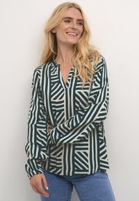 Bluza s dugim rukavima i V-izrezom, ukrašena geometrijskim uzorkom zelenih i krem pruga, izrađena od laganog, glatkog materijala.