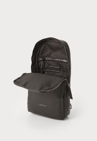Zaino in nylon nero con una texture liscia, dotato di apertura con cerniera e tasca interna, etichetta del marchio in rilievo e design minimalista.