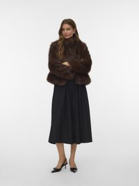 Brun pelsjakke med en blød tekstur, båret over et sort, midtlångt skørt. Sorte hælede sko fuldender looket. Enkelt, elegant design.