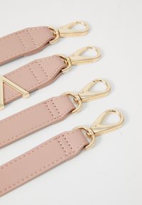 Pink leather straps with gold hardware clips, featuring an angular logo accent and contrasting stitching, displayed against a neutral background.