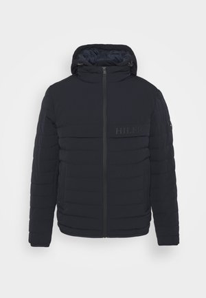 Navy blue puffer jacket with a hood, quilted texture, and front zipper. Features a logo on the chest and elastic cuffs. Lightweight design.