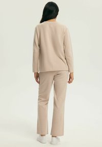 Beżowy dzianinowy top i dopasowane spodnie dzwony, wykonane z miękkiej tkaniny. Top ma okrągły dekolt, a spodnie mają luźny krój o czystym wzornictwie.