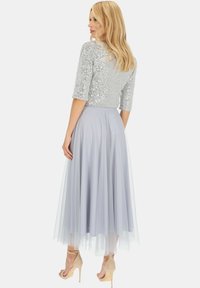 Srebrny top z cekinami i rękawami o długości trzech kwart, w zestawieniu z jasnoszarym tiulowym dołem. Spódnica ma zwiewny krój i długość do kolan, z przezroczystą nakładką.