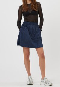 Navyblauwe rok van zachte stof, met een elastische tailleband en zijzakken, gecombineerd met een zwarte doorschijnende top met lange mouwen en sneakers.