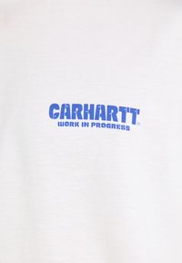White cotton t-shirt featuring a blue "CARHARTT WORK IN PROGRESS" logo. Simple design with a smooth texture and a relaxed fit.