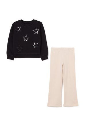 Schwarzer Sweatshirt mit silbernen Sternmustern und langen Ärmeln, kombiniert mit beigen weiten Hosen mit elastischem Bund.
