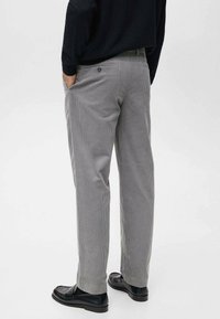 Pantalon en velours côtelé gris, coupe droite, avec une poche arrière à bouton et des poches latérales, porté avec des chaussures noires.