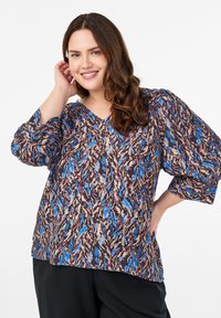 Løs pasform bluse med et levende abstrakt mønster i blå, beige og rød på en mørk baggrund, med puffede ærmer og V-udskæring.