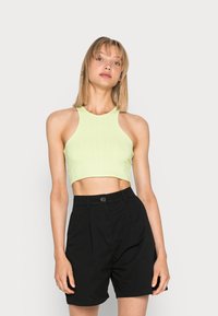 Top cropped canelado verde-claro com gola alta e design sem mangas, combinado com calções pretos ajustados com pregas frontais.