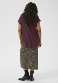 Burgundy short-sleeve top paired with a knee-length skirt featuring a black and cream zebra pattern and side slit, worn with black ankle boots.
