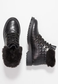 Botas negras acolchadas hasta el tobillo con cuello de piel sintética, puntera redonda, diseño con cordones y suelas robustas con un patrón de dibujo prominente.