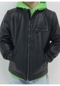 Czarna kurtka z eco-skóry z zamkiem z przodu, bocznymi kieszeniami i pikowanymi akcentami na ramionach. Nosi ją osoba w zielonym kapturze o gładkiej teksturze.