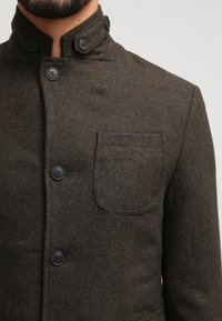 Brauner Wollmischungsblazer mit hohem Kragen, Dreiknopfverschluss und Brusttasche mit Klappen-Detail. Strukturierter Stoff, dezente Farbvariation.
