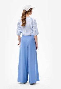 Lichtblauwe wijde broek gecombineerd met een gestreept blauw-wit shirt. De outfit heeft een relaxte pasvorm en is gemaakt van zachte, gladde stof.