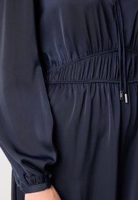 Navy blue dress featuring a soft, smooth texture, gathered waist, and voluminous long sleeves with elastic cuffs and subtle sheen.