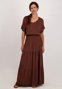 Bruine, gelaagde maxi-jurk gemaakt van lichte stof. Heeft korte mouwen, een v-halslijn en een elastische taille voor een relaxte pasvorm.