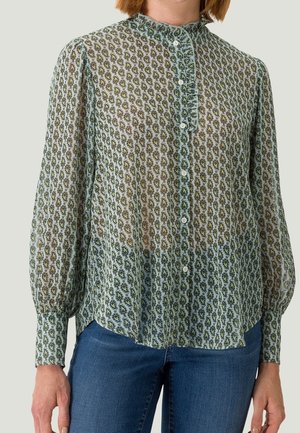 Transparante blouse met lange mouwen en groen paisley-patroon, voor met knopen, gerimpelde kraag, gedragen met een blauwe spijkerbroek.