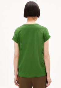 Camiseta verde de manga corta con puños enrollados, material de algodón, corte relajado y un diseño simple, sin adornos, vista desde la parte de atrás.