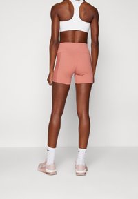 Růžové sportovní šortky s vysokým pasem, spárované s bílým sportovním topem a světlými růžovými teniskami, s hladkým a přiléhavým designem.