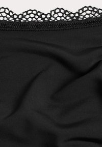 Tela negra con una textura acanalada y un intrincado borde de encaje negro en el borde superior, que muestra un delicado patrón abierto.