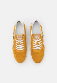 Żółte zamszowe trampki z białymi sznurowadłami, wyposażone w zamek błyskawiczny z boku oraz perforowaną fakturę. Zawierają logo na języku.